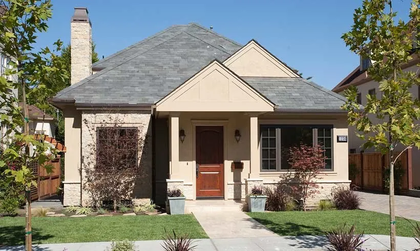 Front of a Burlingame residence with beige stucco, a stone base, a slate roof, a wood door, and a columned porch.