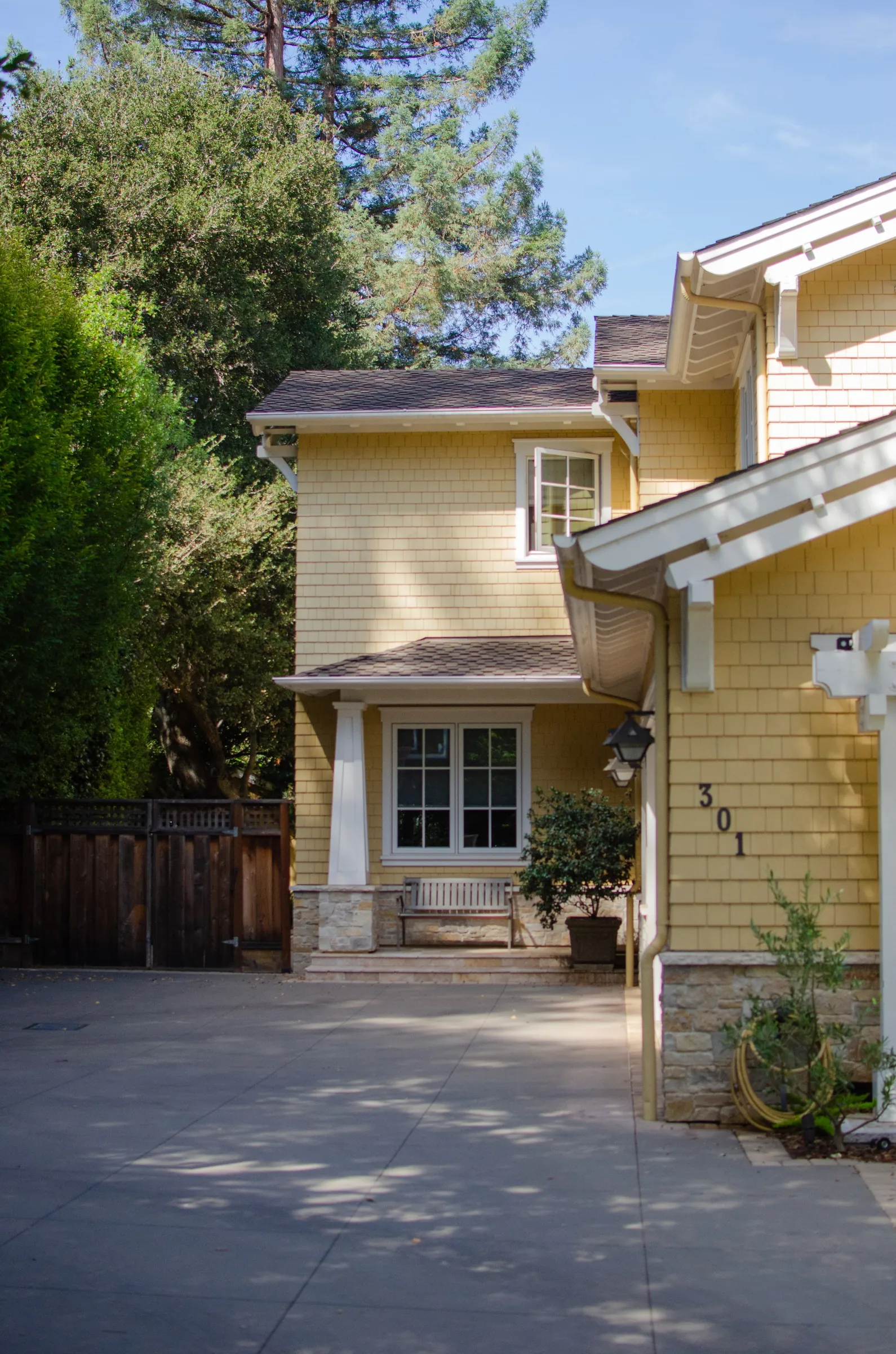 Side of a Menlo Park residence with yellow shingle siding, white trim, a stone base, and a covered side window.