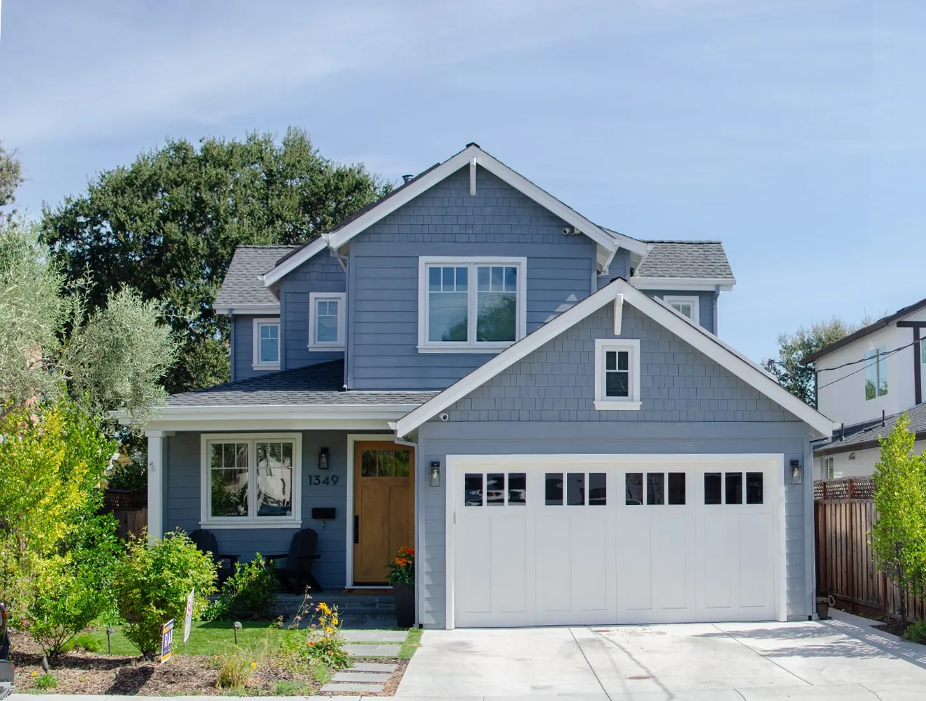 Front of a San Carlos residence with blue shingle siding, white trim, a wood entry door, and a white garage door.