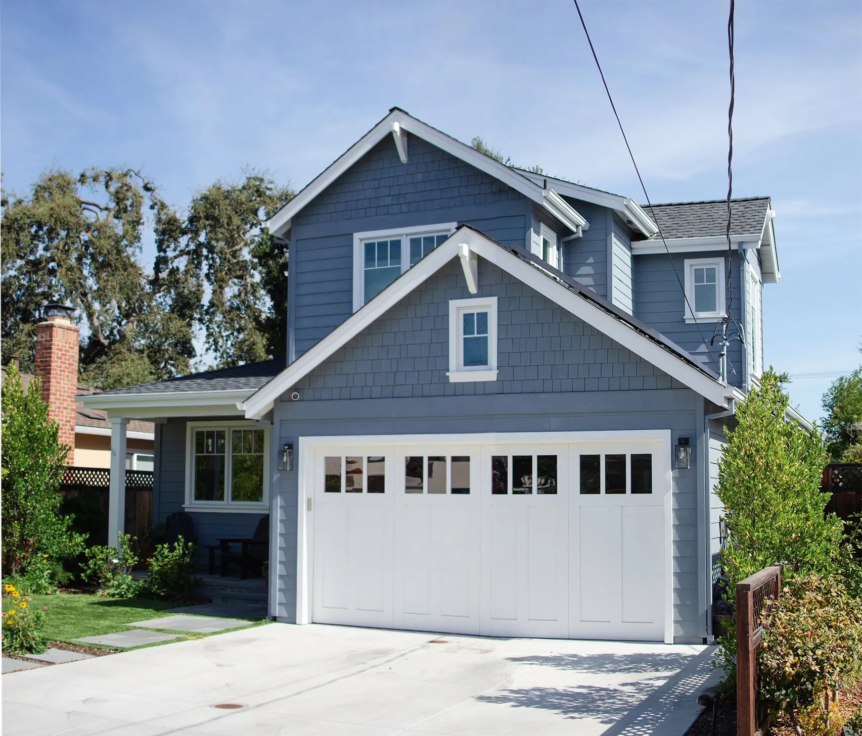 Wide front view of a San Carlos residence with blue shingle siding, white trim, a gabled garage, and a white garage door.