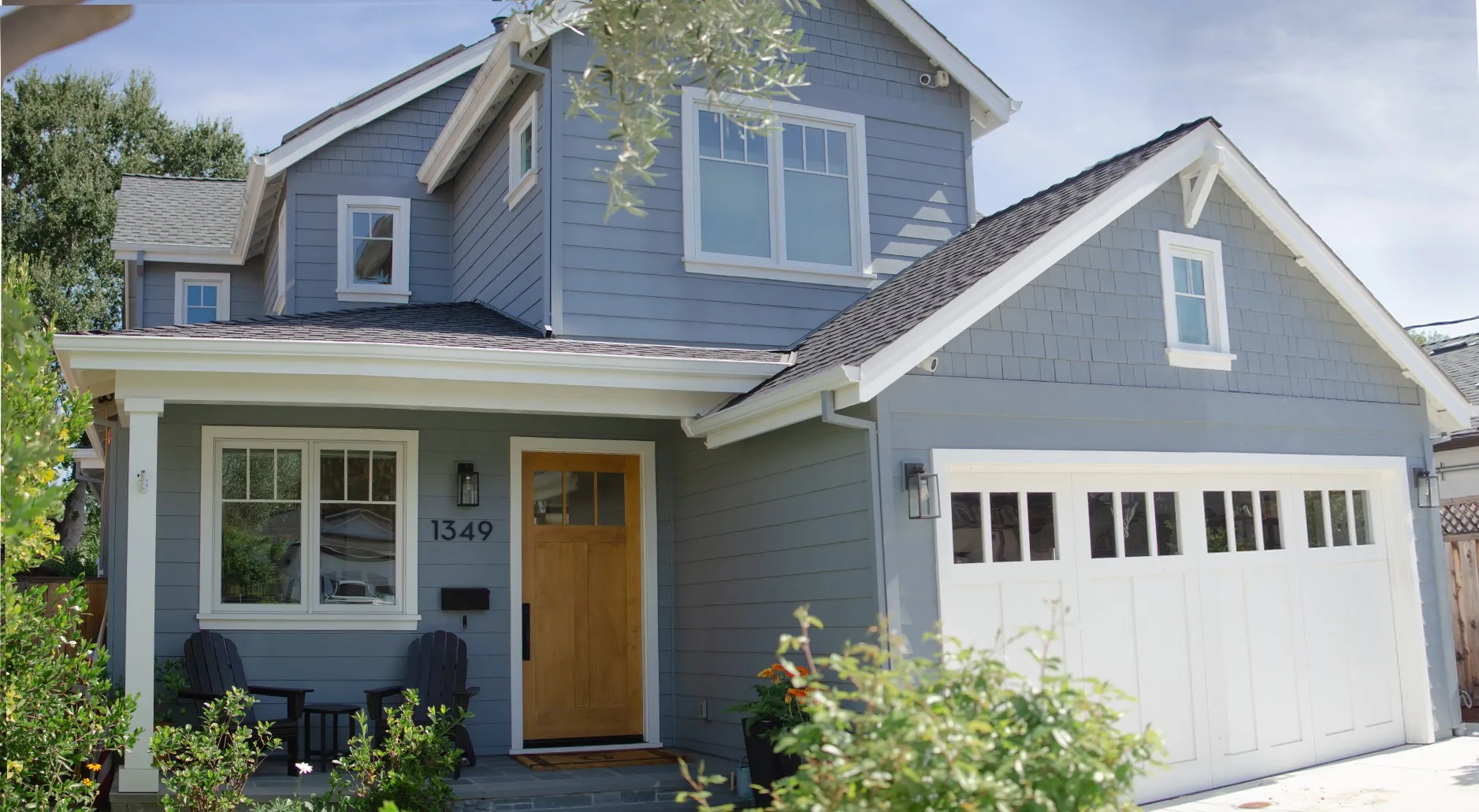 Closer front view of a San Carlos residence with blue siding, white trim, a wood entry door, a covered porch, and a white garage door.